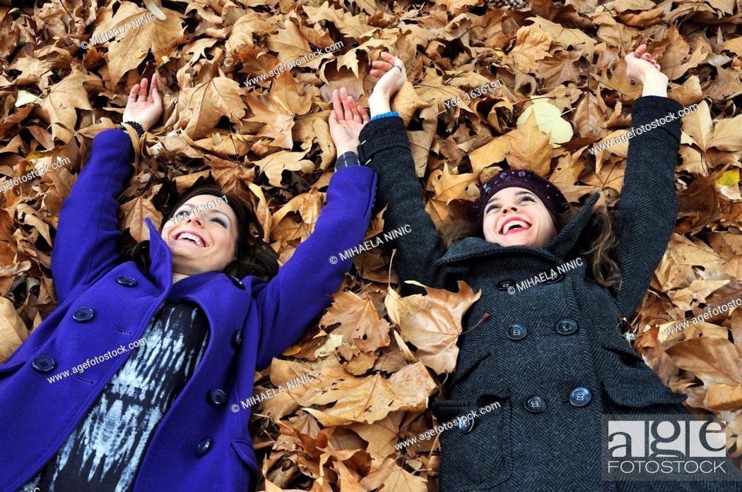 Stock Photo: Portrait of a two young woman lying on autumn leaves from a bird's eye view laughing and having fun.