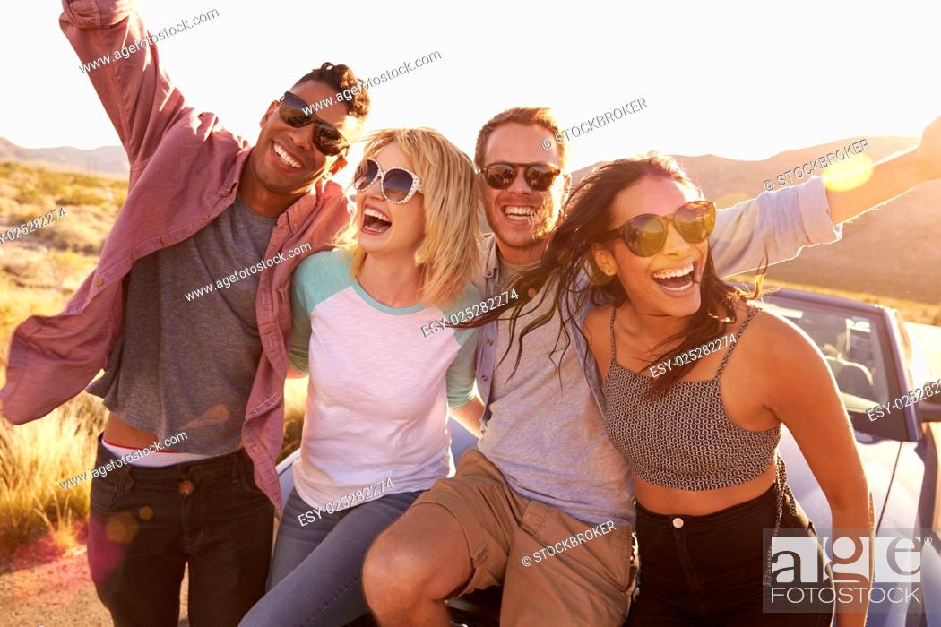 Stock Photo: Friends On Road Trip Sitting On Hood Of Convertible Car.