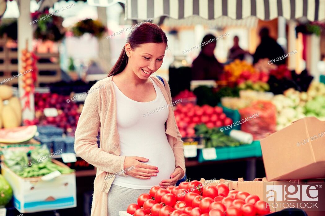Stock Photo: sale, shopping, food, pregnancy and people concept - happy pregnant woman choosing tomatoes at street market.