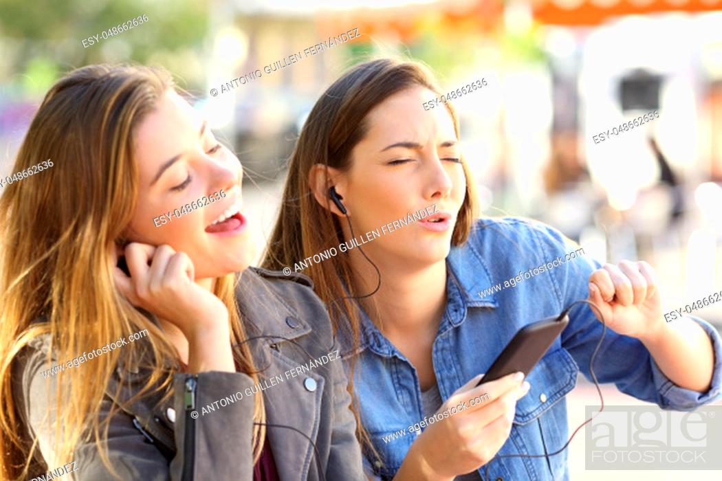 Stock Photo: Joyful friends listening to music on line from a smart phone and singing sharing earphones in the street.