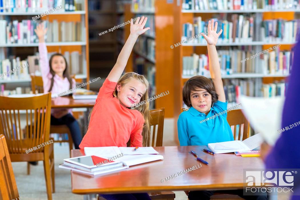 Stock Photo: Students raising their hands in library.