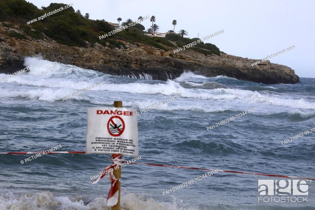 Stock Photo: 02 September 2021, Spain, Manacor: A sign prohibits swimming on the beach of Cala Mendia in Manacor on Mallorca. Two young holidaymakers from North.