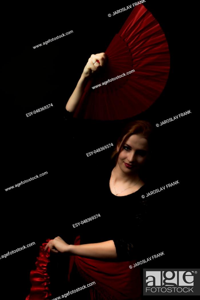 Imagen: Low Key portrait of young woman dancing flamenco holding red fan over head. All on the dark background.