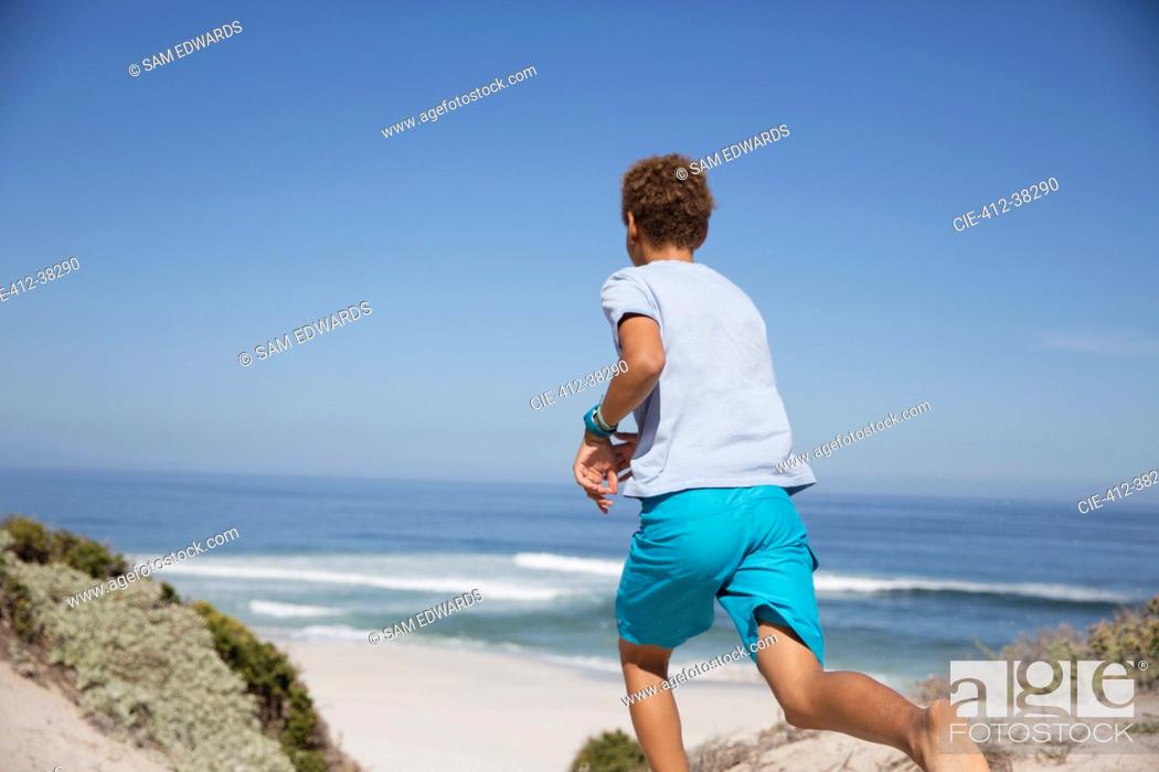 Stock Photo: Pre-adolescent boy running on sunny summer ocean beach.