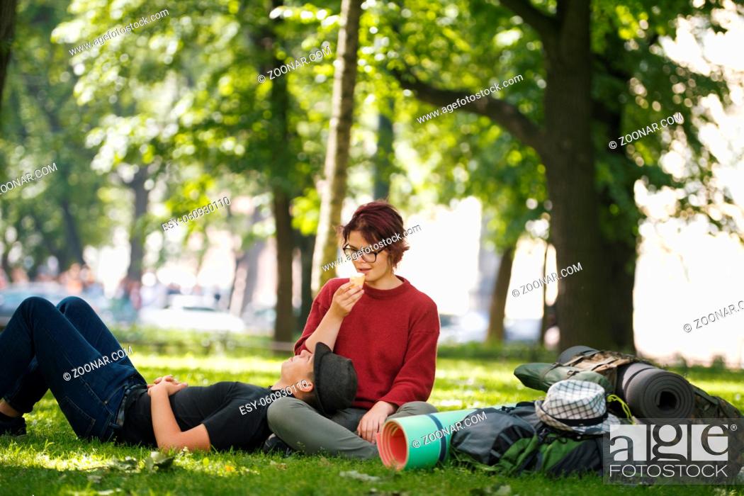 Photo de stock: Couple of teenagers tourists with backpacks have rest in the city park, telephoto shot.