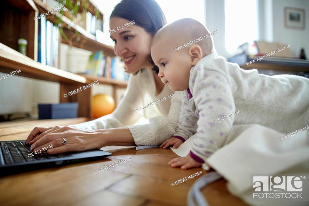 Stock Photo: Baby daughter watching mother typing on laptop on floor.