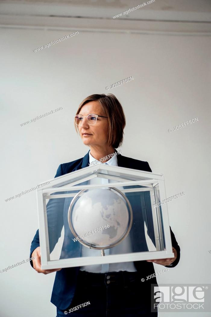 Stock Photo: Businesswoman with globe in house shaped glass container.