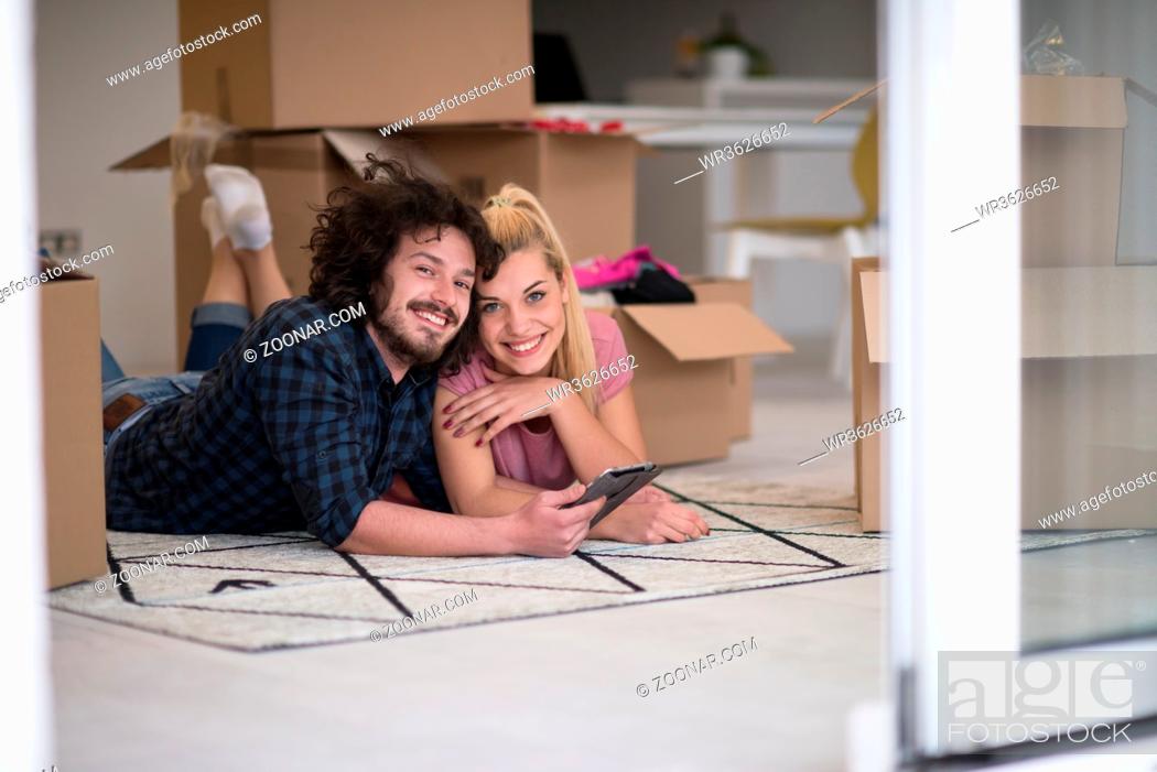 Stock Photo: Young couple in love moving in a new flat, lying on the floor and surfing the web on a tablet computer in search of new redecoration ideas.