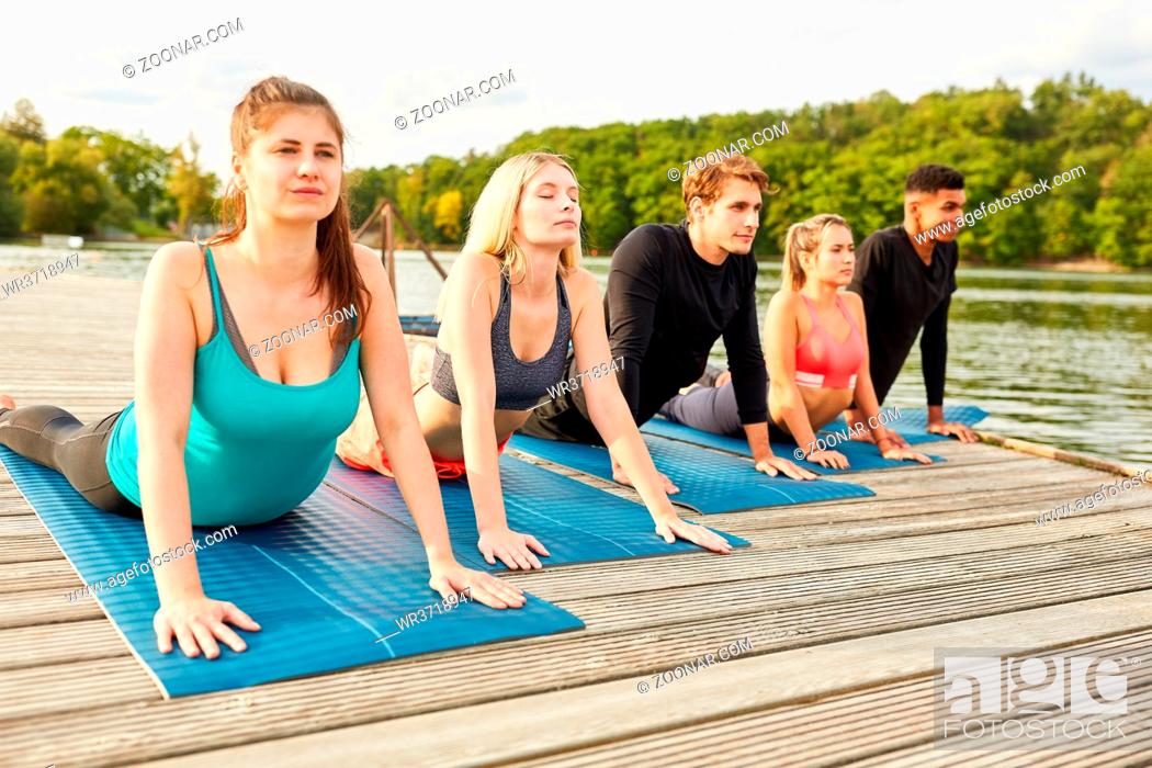 Stock Photo: Gruppe junger Leute macht eine Dehnungsübung beim Sonnengruß im Yoga Kurs.