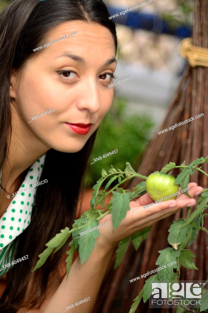 Stock Photo: Portrait of young woman looking at camera and green tomato on her hand.