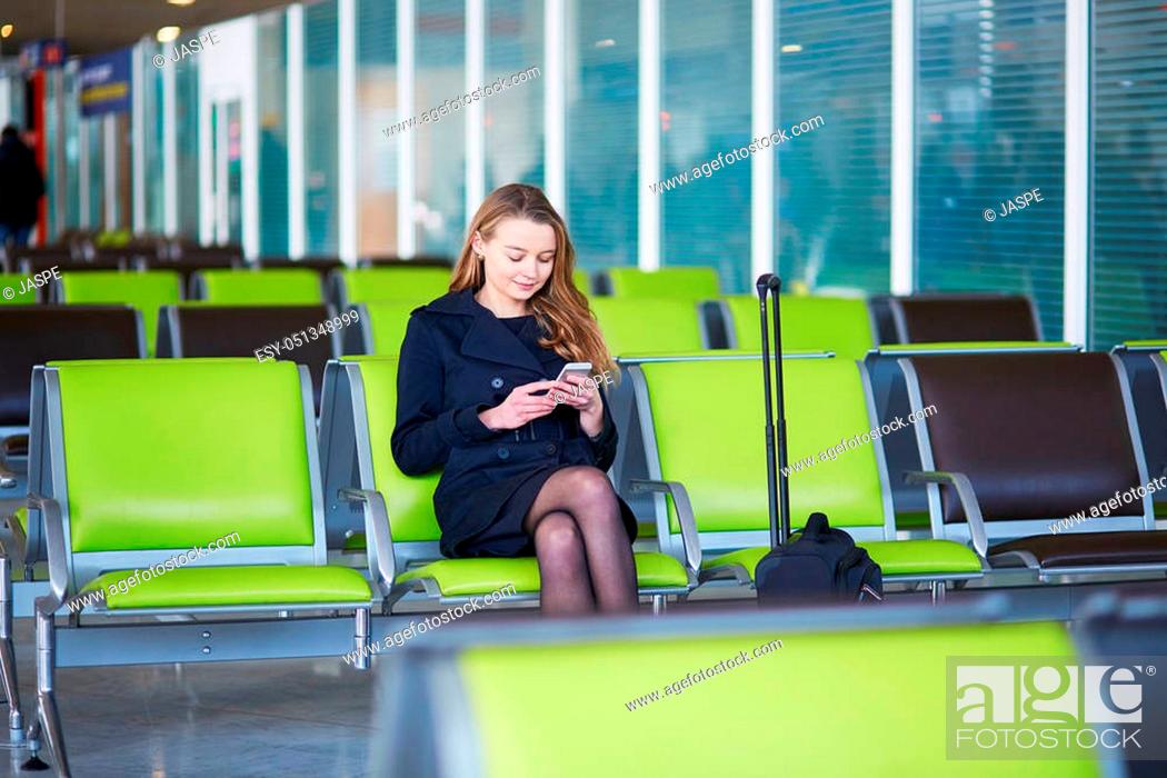 Stock Photo: Young woman in international airport, checking her phone while waiting for her flight.