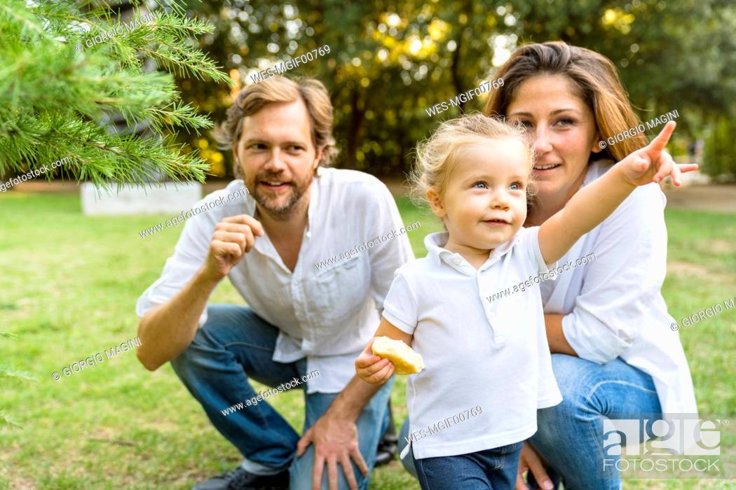 Stock Photo: Parents with little daughter pointing her finger on a meadow.