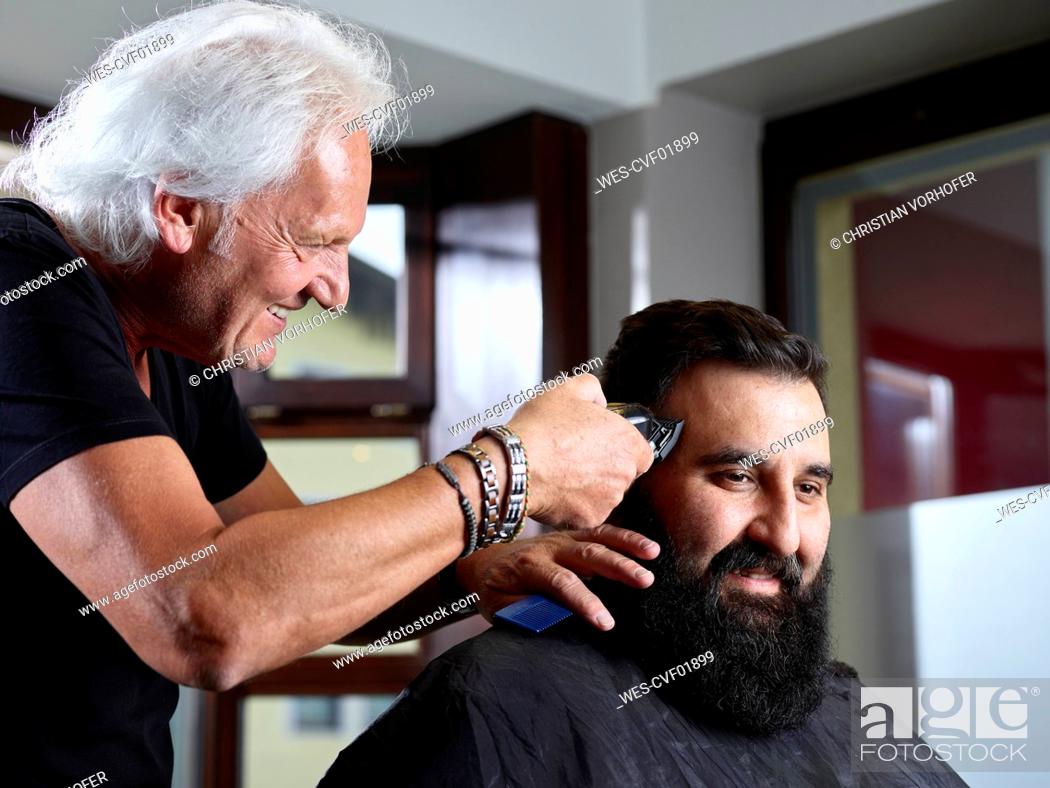 Stock Photo: Smiling hairstylist cutting man's hair using electric razor at salon.