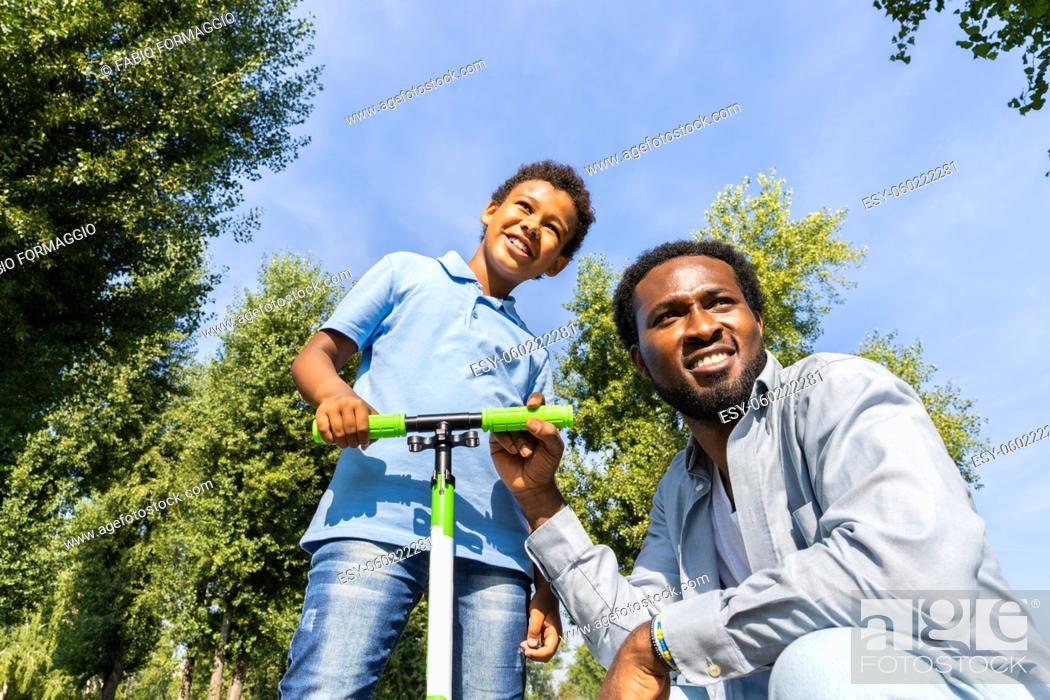 Stock Photo: Beautiful happy african american family bonding at the park - Black family having fun outdoors, dad teaching son to ride on scooter.