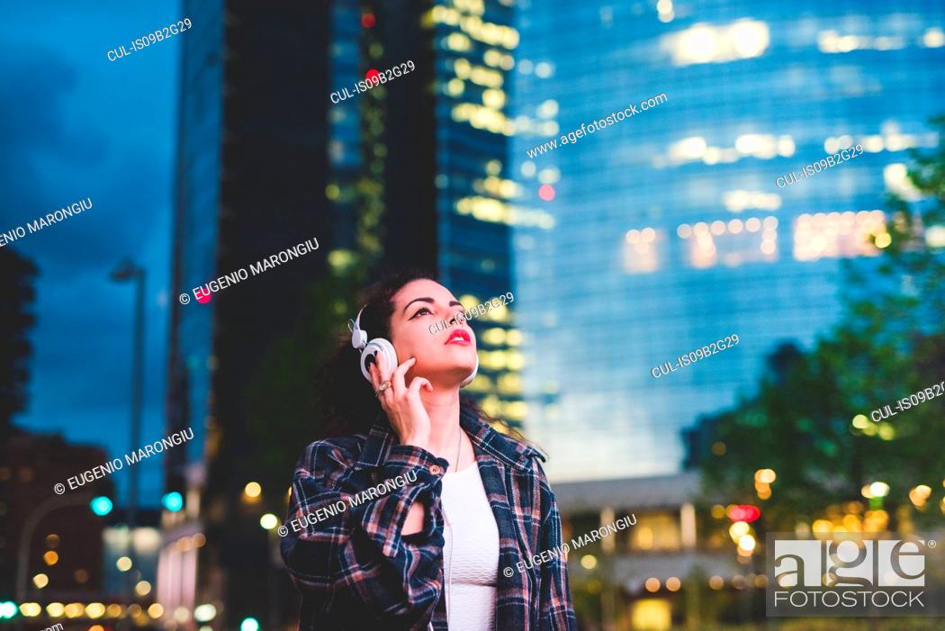 Stock Photo: Woman wearing headphones in the city looking up, Milan Italy.