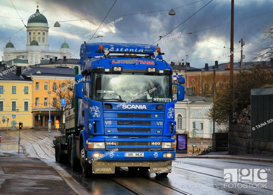 Stock Photo: Blue customised Scania 144G A. Street Trans pulling gooseseck trailer to Katajanokka Harbour. On the background, Helsinki city, Finland. April 3, 2020.