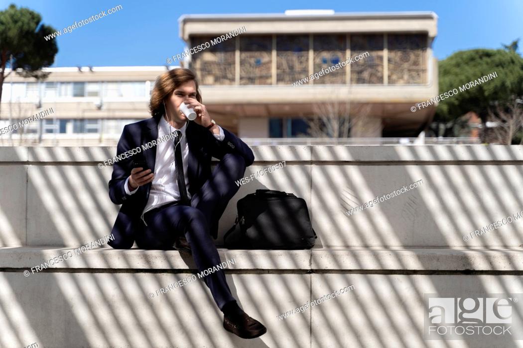 Stock Photo: Italy, Florence, young businessman using smartphone with earbuds outdoor.