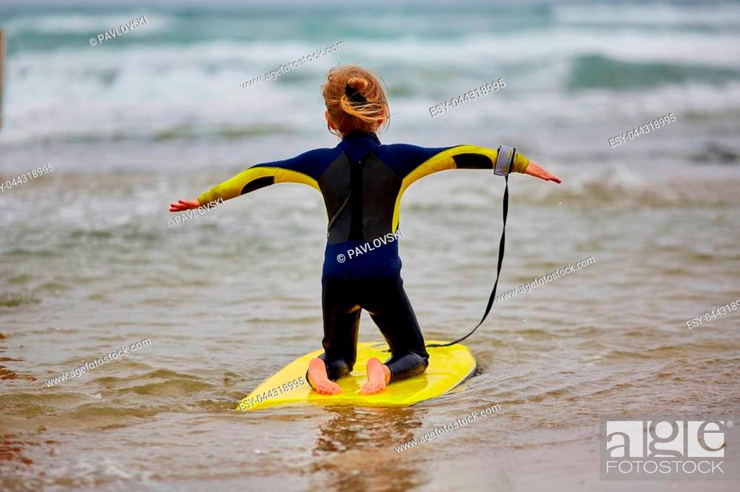 Stock Photo: a five year old surfer girl is sitting on the sand.