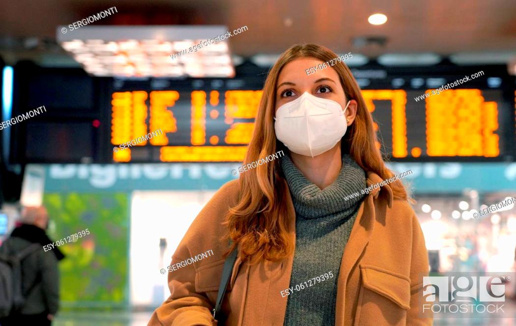 Stock Photo: Business woman wearing face mask FFP2 KN95 at train station and keeping social distance. Young woman waiting for the train with timetables on background.