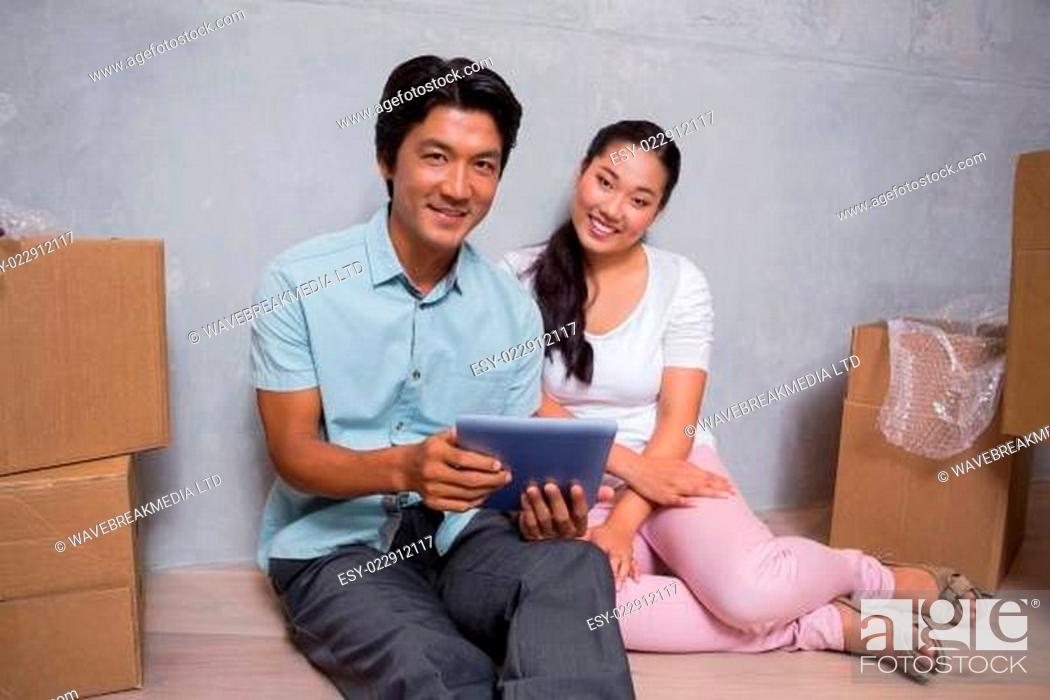 Stock Photo: Happy couple sitting on floor using tablet surrounded by boxes.