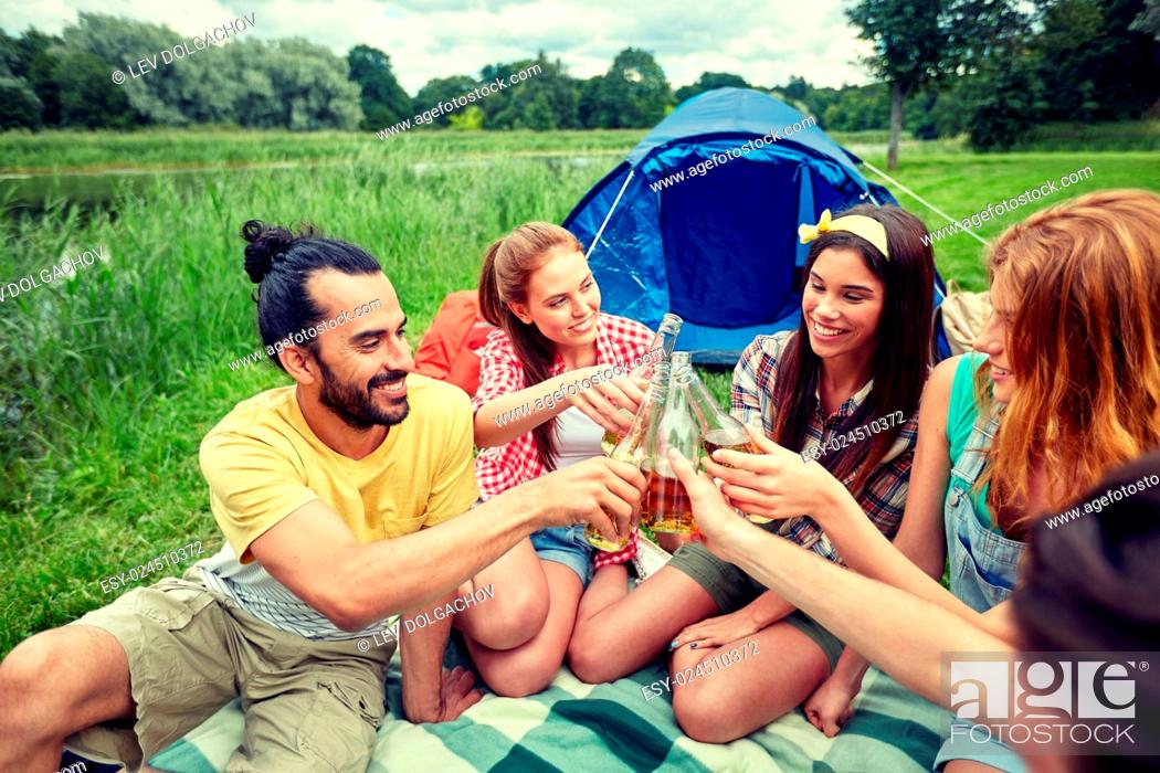Stock Photo: camping, travel, tourism, hike and people concept - happy friends with glass bottles drinking cider or beer at campsite.