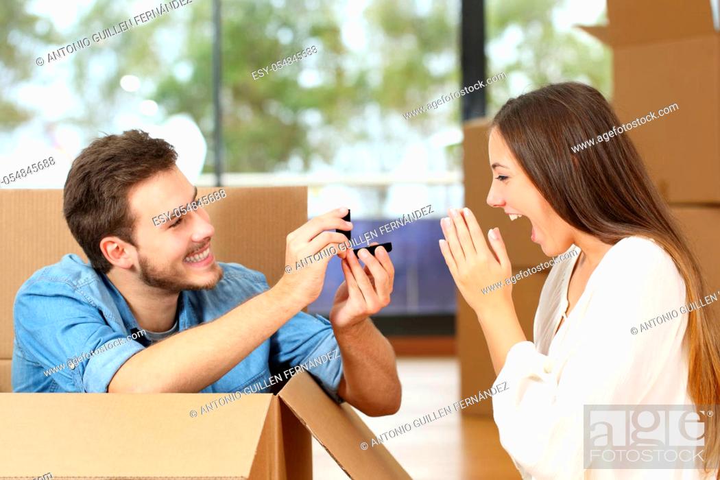 Stock Photo: Happy man proposing to excited girlfriend with wedding ring while moving at new home surrounded by boxes.