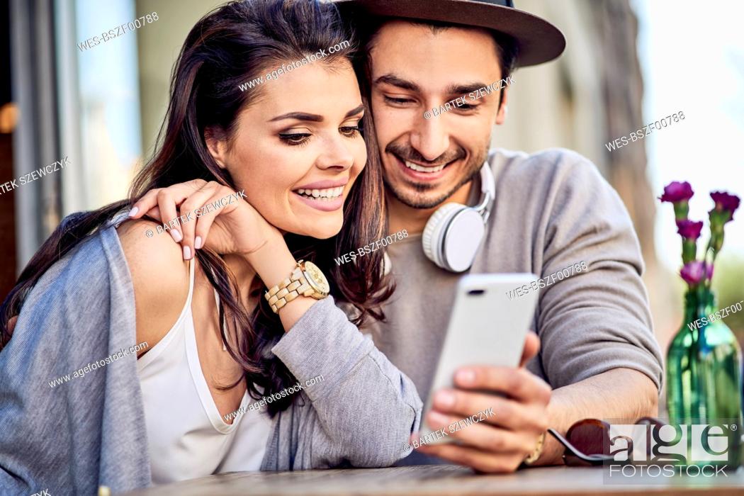 Stock Photo: Happy young couple using cell phone at outdoors cafe.
