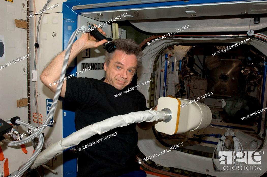 Stock Photo: Canadian Space Agency astronaut Robert Thirsk, Expedition 2021 flight engineer, gives himself a haircut and uses a vacuum cleaner to collect floating hairs.