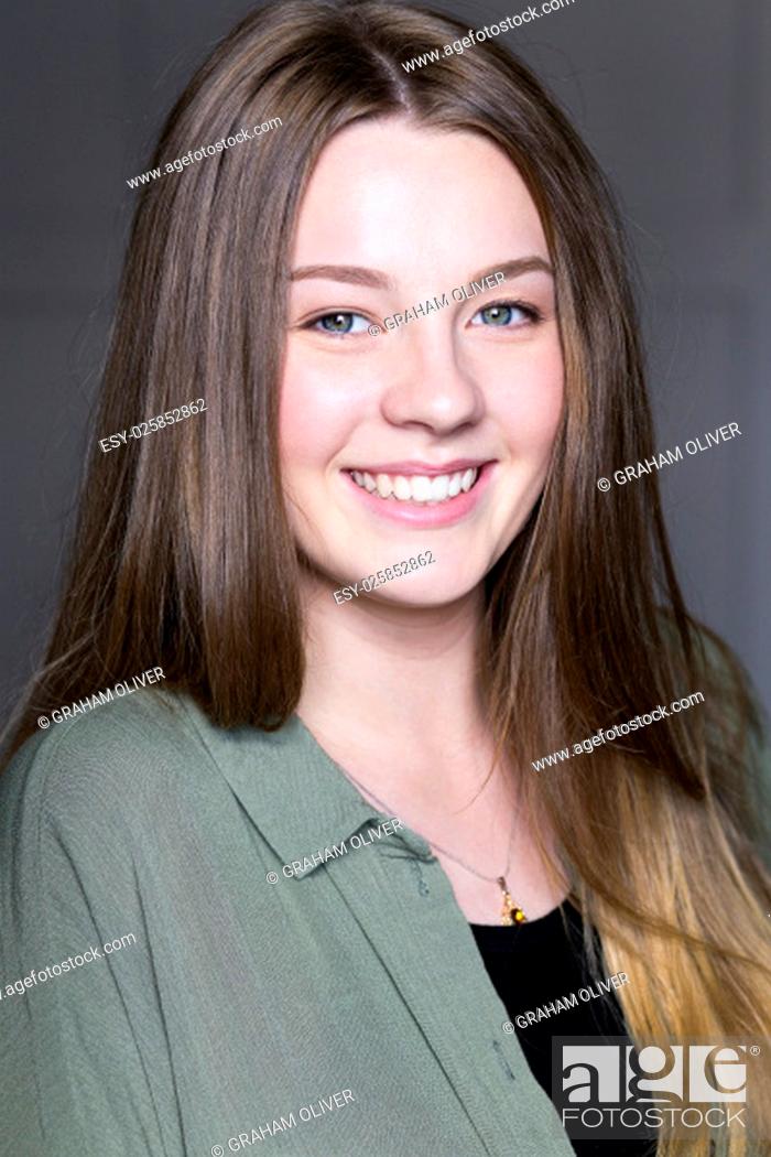 Stock Photo: Headshot of a beautiful young woman taken in a studio on a grey background. She is wearing casual clothing and looking at the camera and smiling.