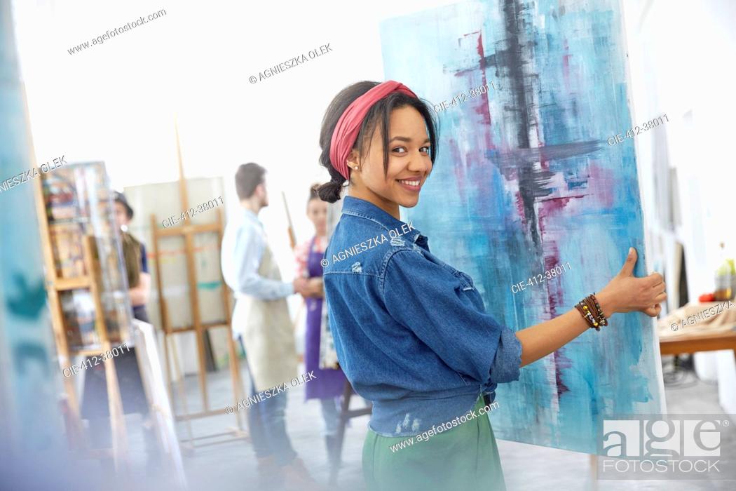 Stock Photo: Portrait smiling female artist lifting painting in art class studio.
