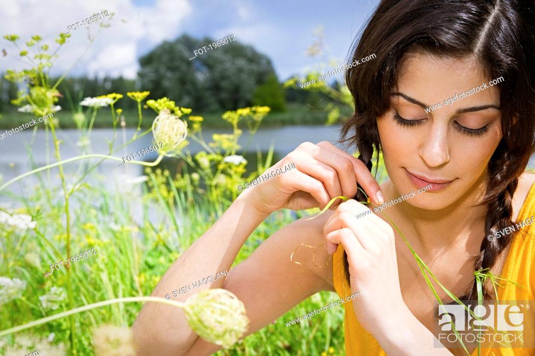 Stock Photo: Beautiful young woman braiding hair in sunny meadow.