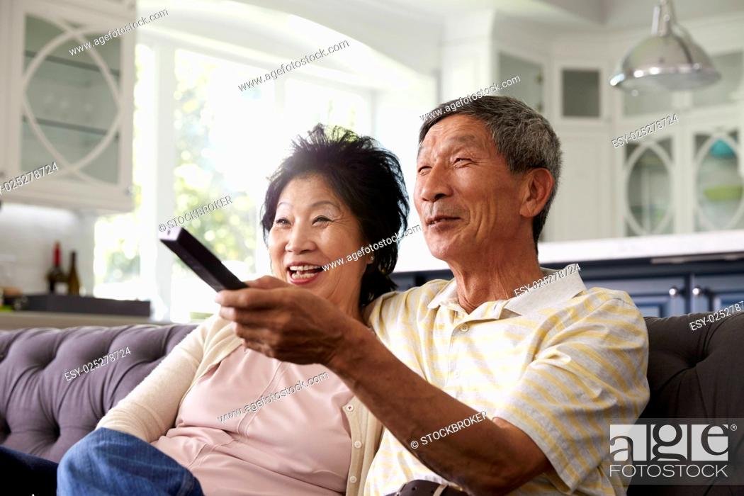 Stock Photo: Senior Asian Couple At Home On Sofa Watching TV Together.