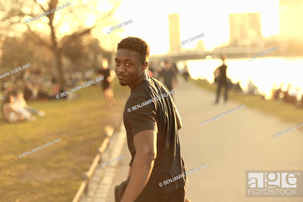 Imagen: African man looking backwards over shoulder, running next to river Main, in Frankfurt, Germany.