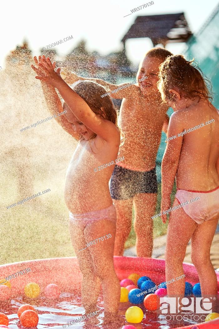 Stock Photo: Little cute adorable kids enjoying a cool water sprayed by their father during hot summer day in backyard. Candid people, real moments, authentic situations.