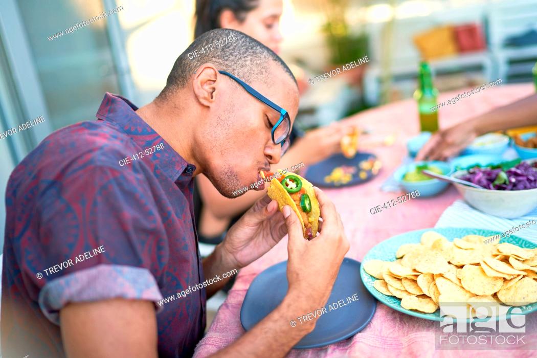 Imagen: Young man eating taco at patio table.
