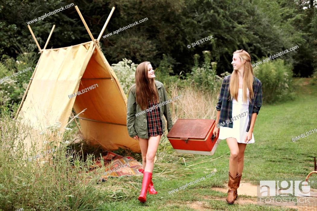 Photo de stock: Women carrying vintage cooler near camping tent in forest.