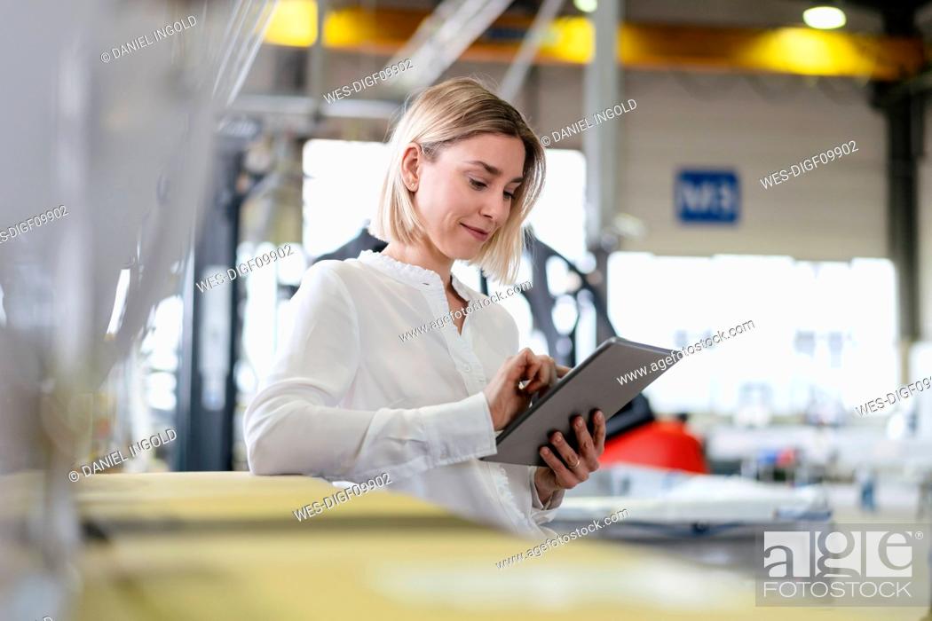 Stock Photo: Smiling young woman using tablet in a factory.