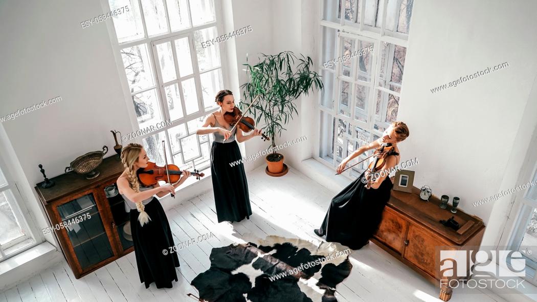 Stock Photo: Three Women In Beautiful Dresses Are Playing Musical Instruments Inside Large And Bright Room With Big Windows.