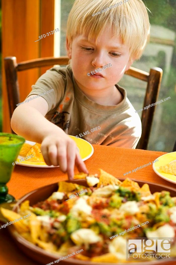 Stock Photo: Boy eating nachos with tomato salsa and guacamole.