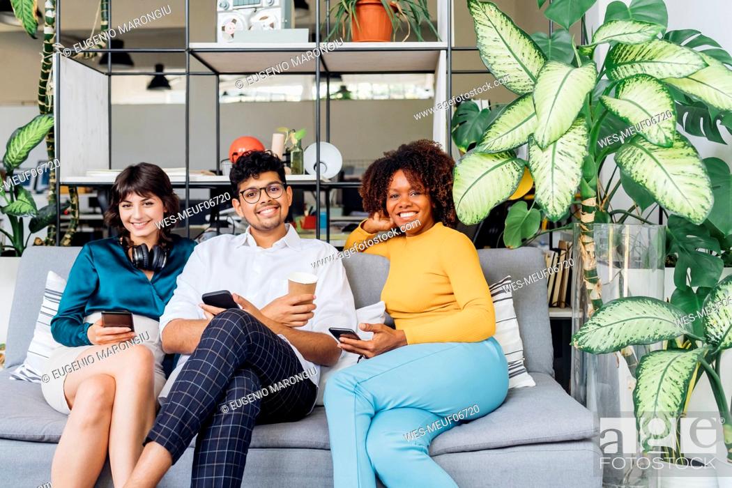 Photo de stock: Smiling multiracial colleagues with smart phones on sofa in office.