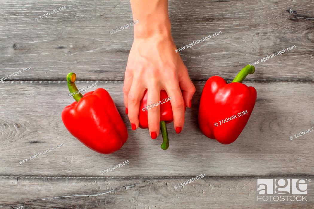 Stock Photo: Table top view - gray wood desk and woman hands placed on red bell pepper, with two more at each side.