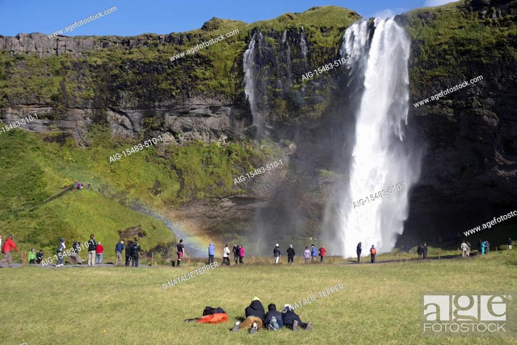 Stock Photo: A stunning landscape of a large waterfall called Seljalandsfoss Waterfall , in Iceland, surrounded by fields and mountains, and crowds, and a rainbow.