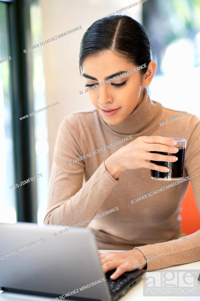 Stock Photo: Young woman having a drink and using laptop in a cafe.