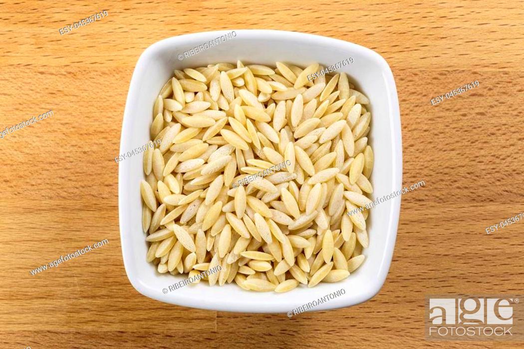 Stock Photo: Overhead shot of raw pearl barley in a white bowl on a wooden chopping board background. Arborio rice is the main ingredient of the traditional Italian Risotto.