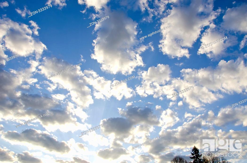 Stock Photo: background of cloudy blue spring sky sunlit by sun and some tree tops in distance.