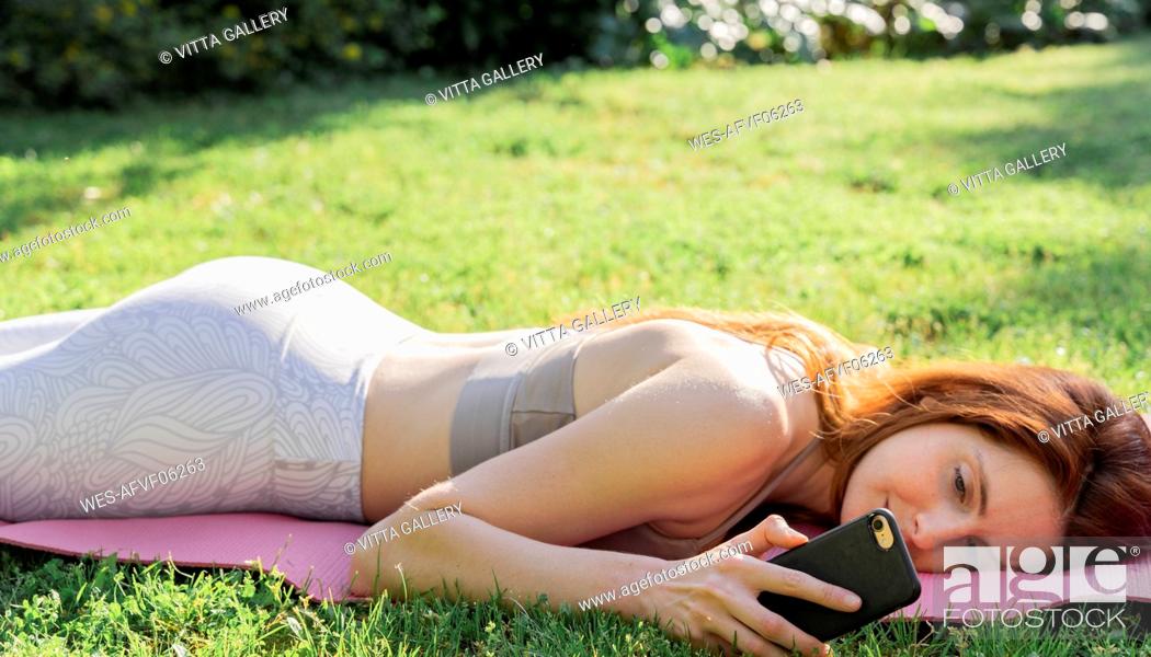 Stock Photo: Young woman lying on a mat in grass checking cell phone.
