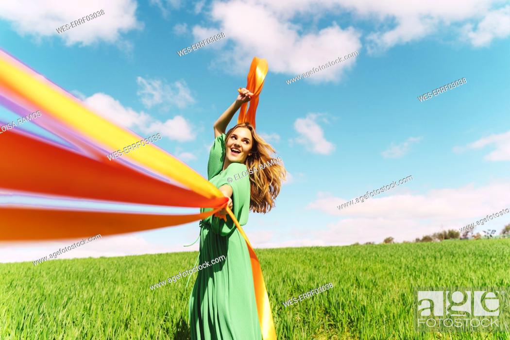 Stock Photo: Happy young woman wearing a green dress in a field with blowing ribbons.