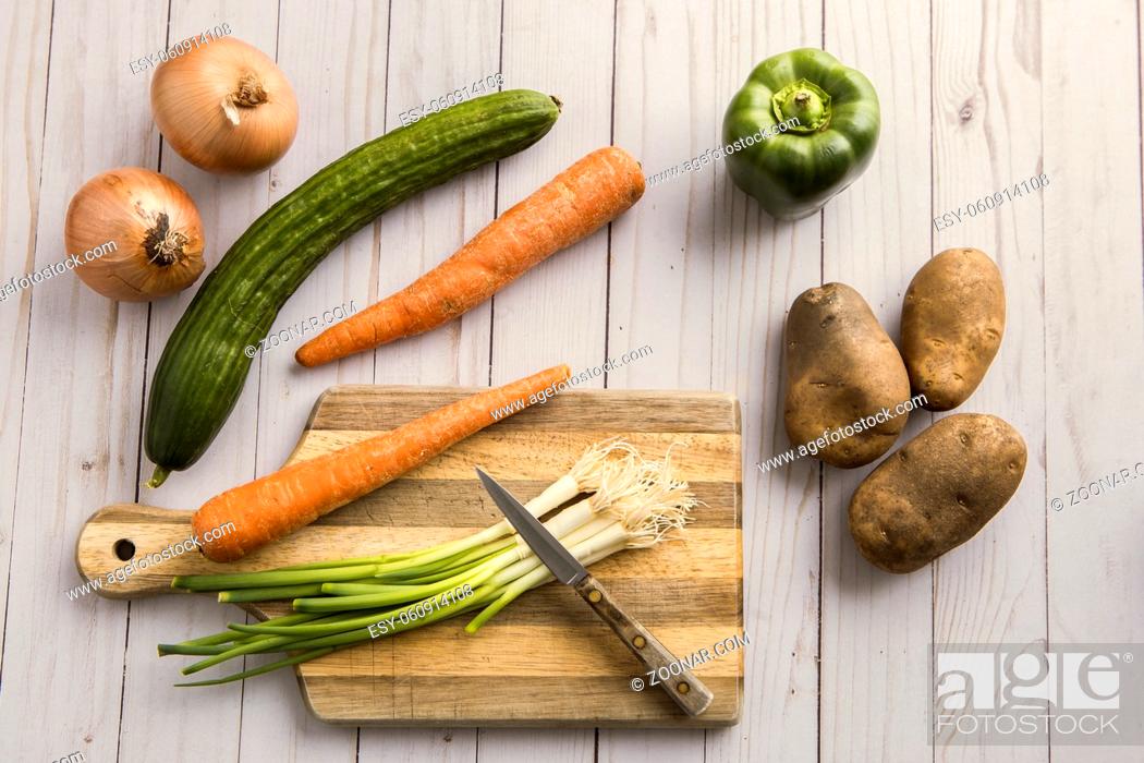 Stock Photo: An assortment of vegetables such as onions, carrots, potatoes, and green bell pepper and a cutting board.