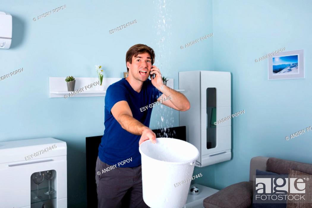 Stock Photo: Worried Man Calling Plumber While Leakage Water Falling Into Bucket At Home.