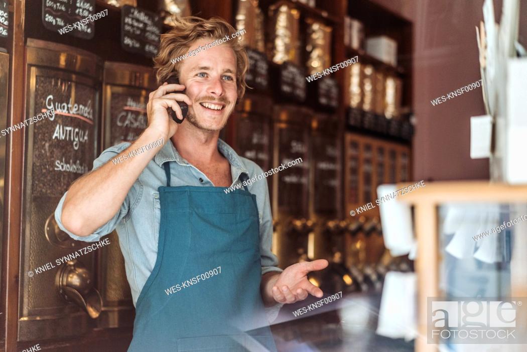 Stock Photo: Smiling coffee roaster in his shop on the phone.